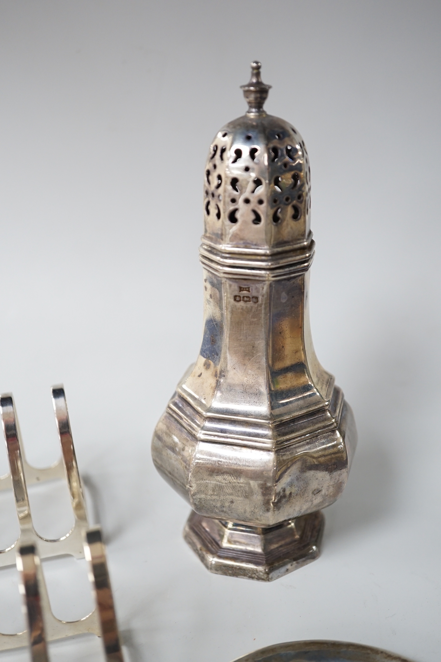 A George V octagonal silver caster, Sheffield 1932, 121 grams, a pair of Walker & Hall toast racks, Birmingham 1921, 101 grams and a trinket dish, decorated with waterlilies, Birmingham 1909, 18 grams
